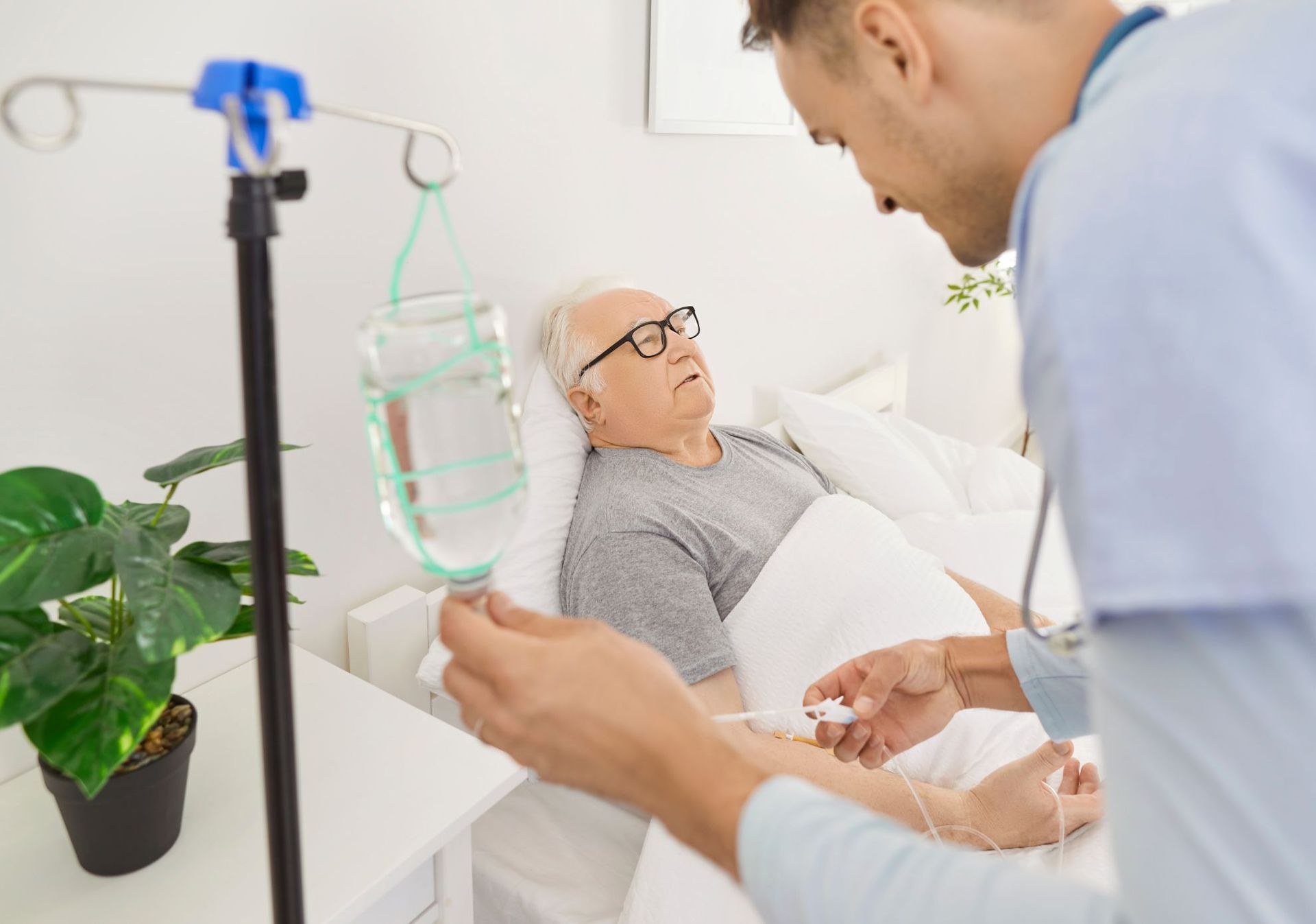 A nurse adjusts an IV drip for a patient resting in a hospital bed.