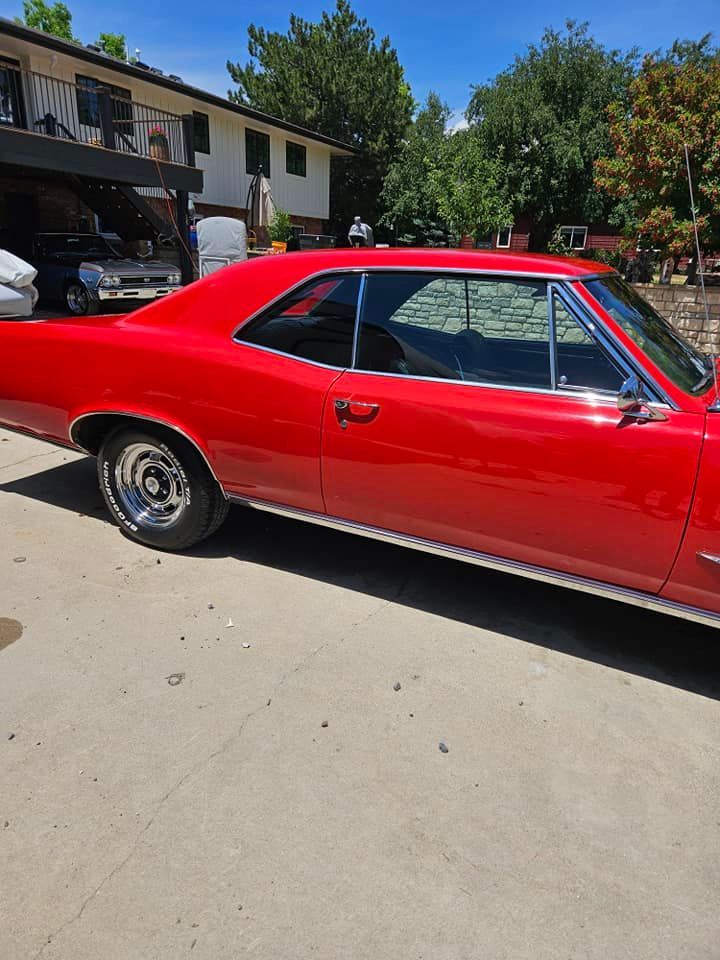 A glossy red vintage coupe car parked on a concrete driveway in front of a house.