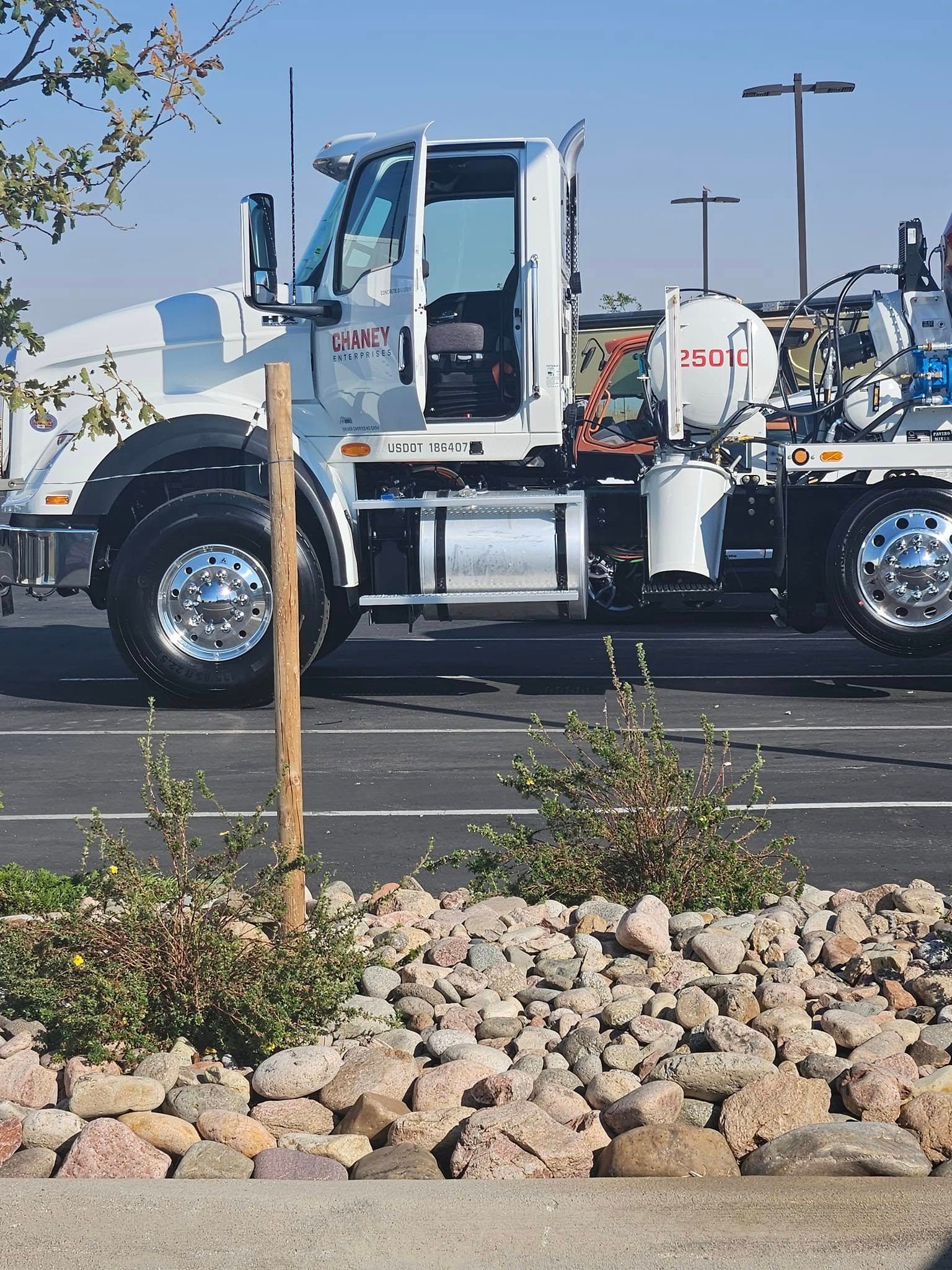 A white utility truck parked in a paved lot behind a stone-filled landscape area with a single wooden post.