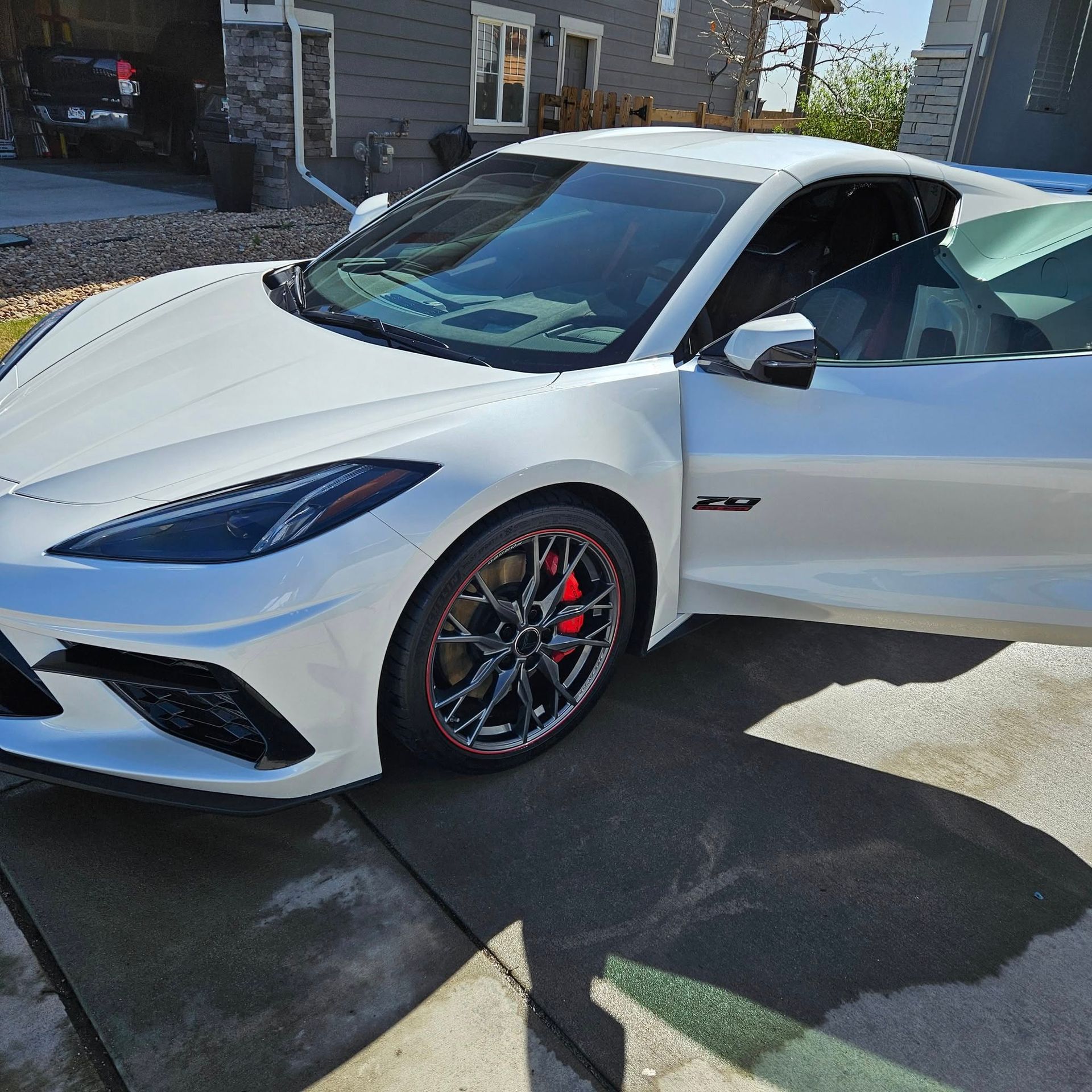 A white Chevrolet Corvette C8 parked in a residential driveway with its driver-side door open.
