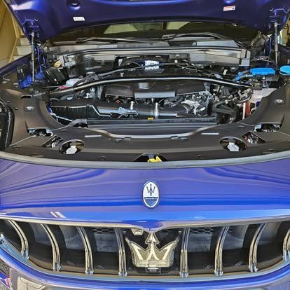 A blue Maserati with its hood open, revealing the engine bay and the brand's trident emblem on the front grille.