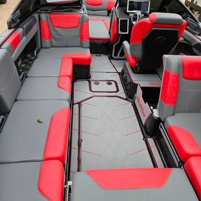 The interior of a boat featuring grey and vibrant red cushioned seating, a central walkway, and a driver’s helm.