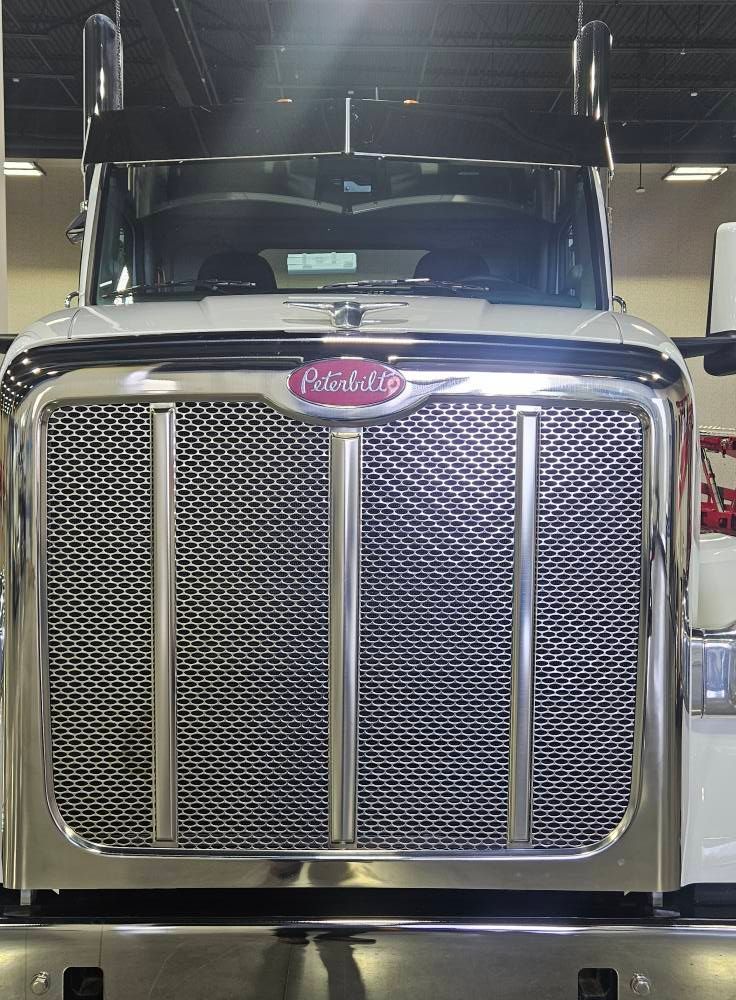 Front view of a white Peterbilt semi-truck, featuring a prominent chrome grille and hood emblem in an indoor setting.