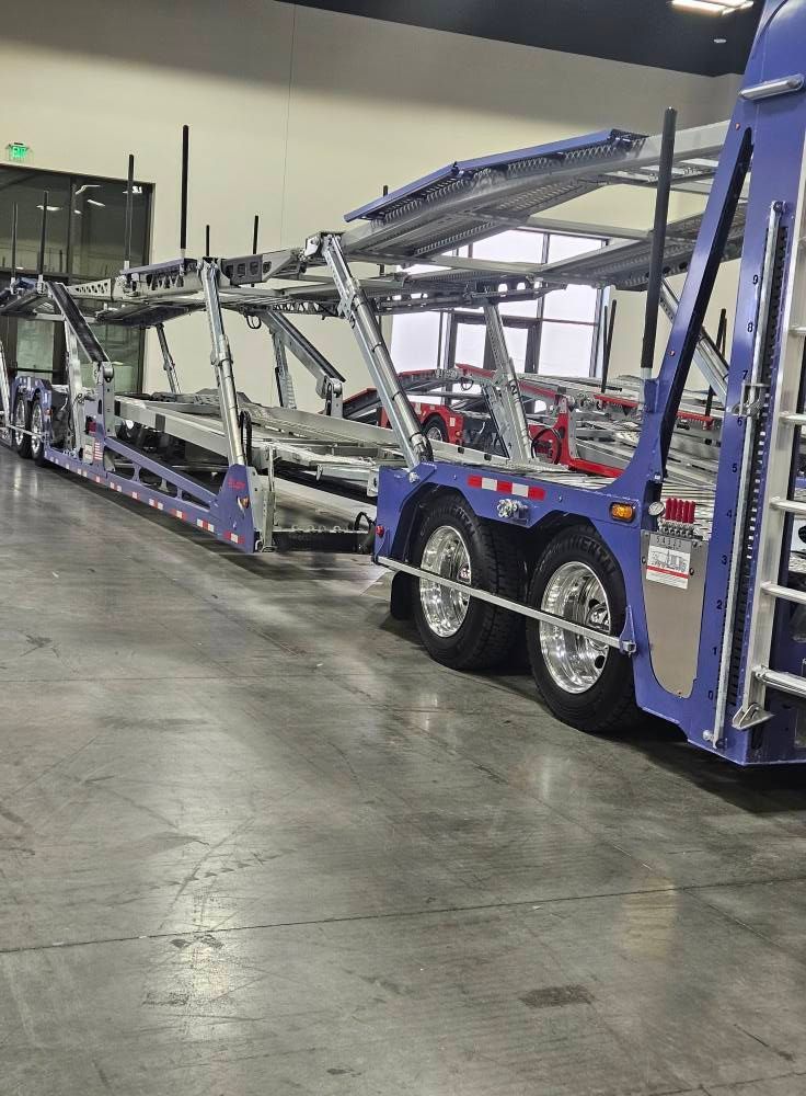 A blue car hauler trailer parked inside a warehouse on a concrete floor.