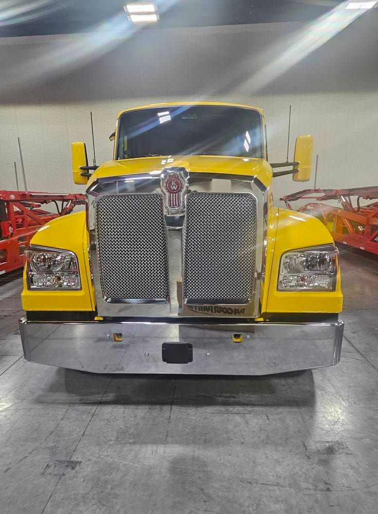 A bright yellow Kenworth semi-truck, viewed from the front, parked inside a spacious warehouse.