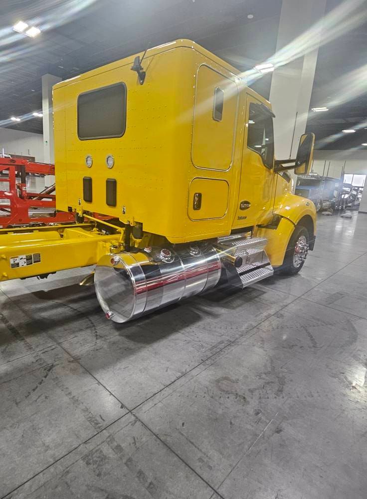 A bright yellow semi-truck cab with a shiny chrome fuel tank, parked inside a spacious warehouse.