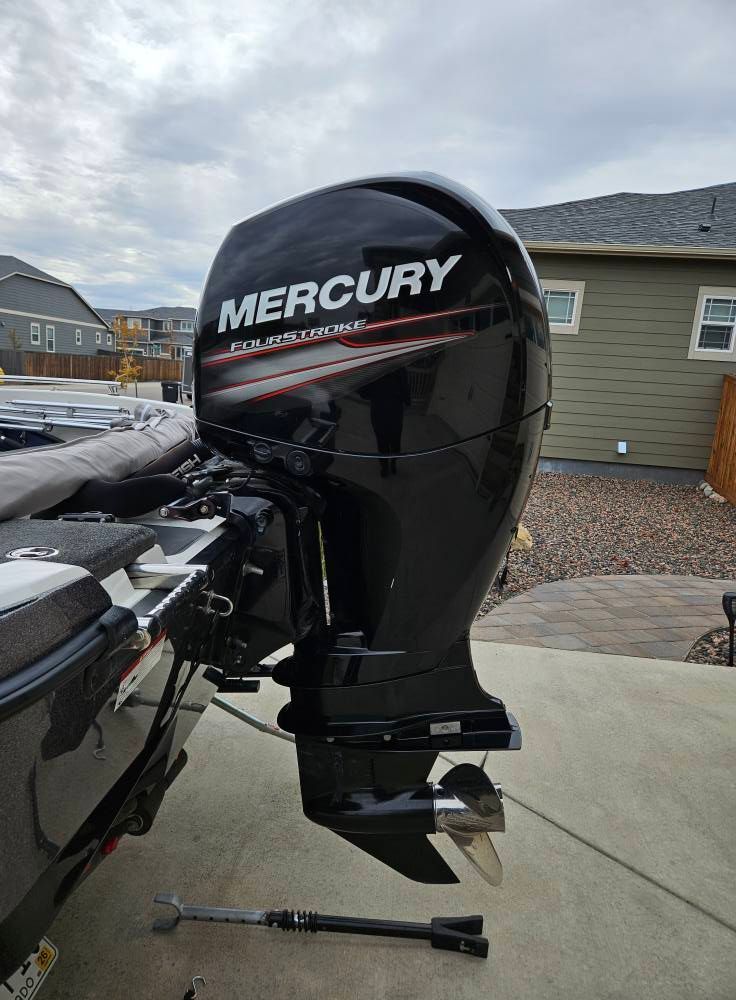 A side profile of a black Mercury outboard boat motor mounted on the back of a boat parked on a paved driveway.