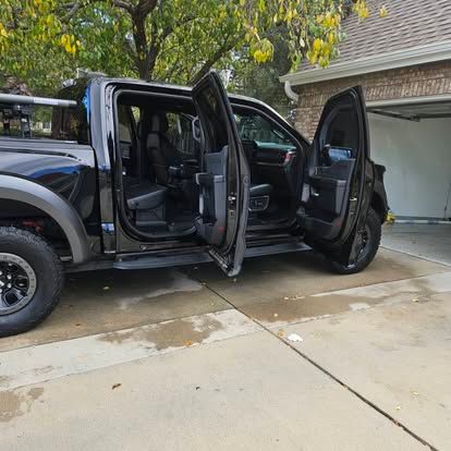 A black pickup truck parked in a driveway with both its driver and passenger side doors open.