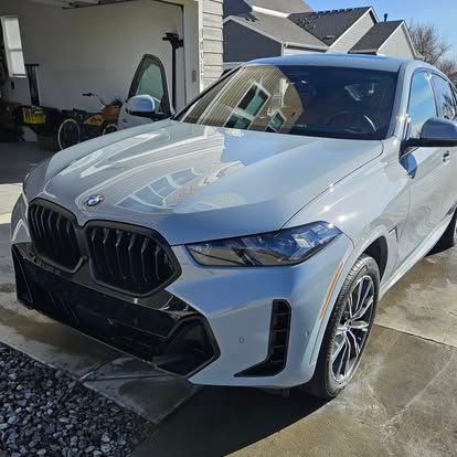 A light gray BMW X6 SUV parked in a residential driveway on a sunny day.