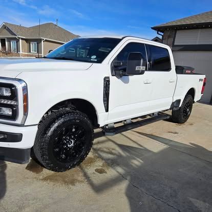 A white Ford Super Duty truck parked on a concrete driveway in front of a house under a clear blue sky.