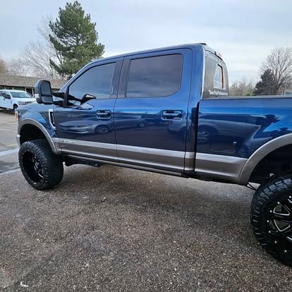 A blue Ford Super Duty pickup truck with two-tone paint and lifted tires parked outdoors.