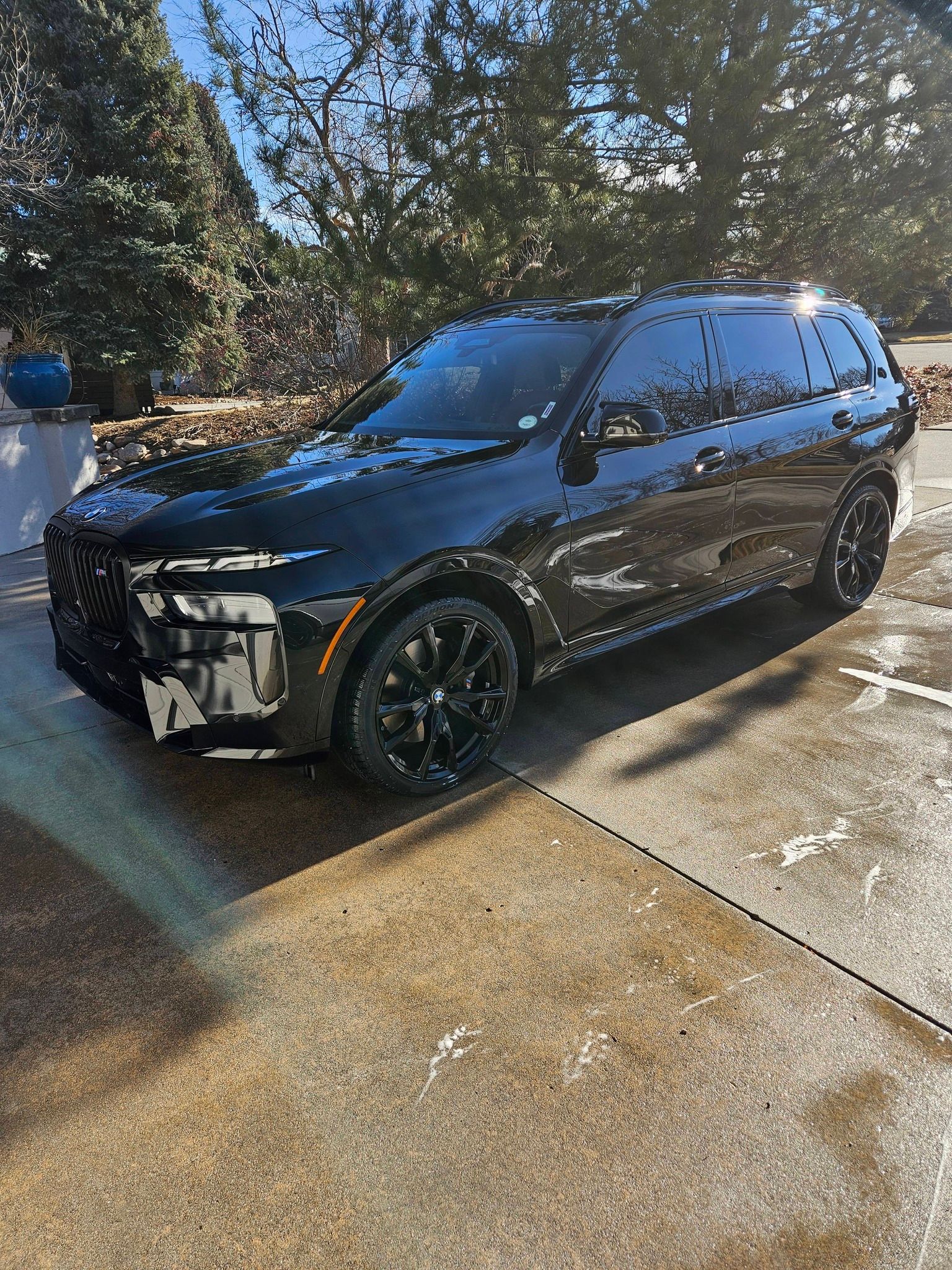 A shiny, black Jeep Grand Cherokee parked on a concrete driveway under bright, sunny skies.