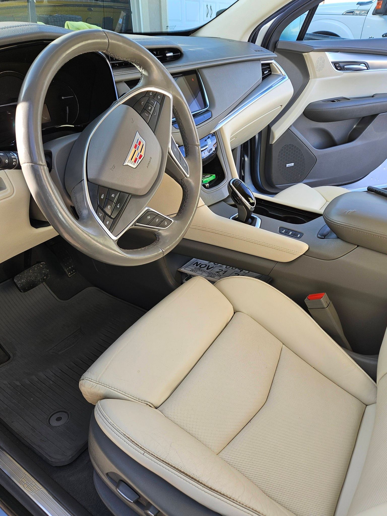 A light-colored leather interior of a Cadillac vehicle, showing the steering wheel, driver’s seat, and dashboard console.
