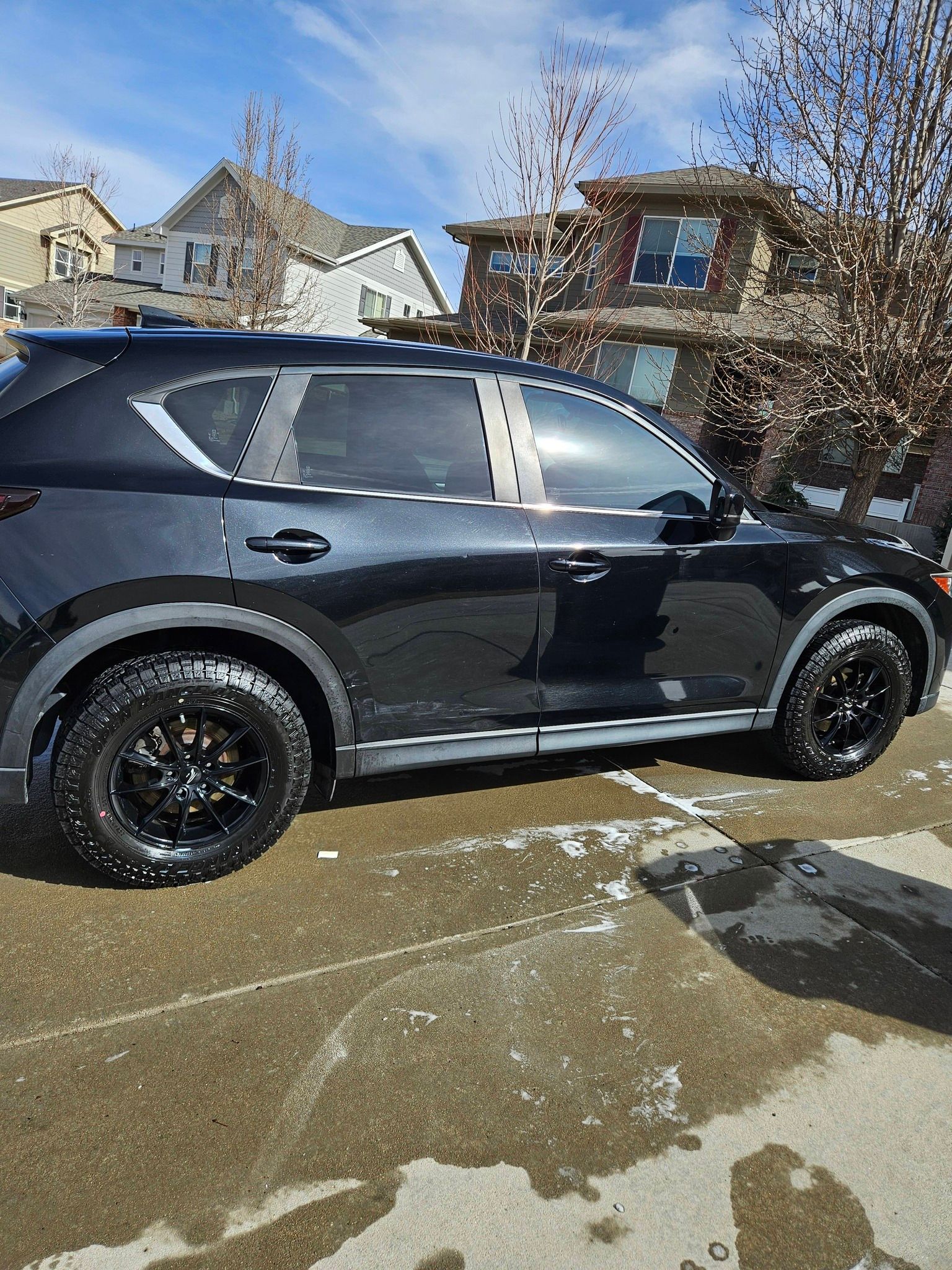 A black SUV parked on a residential driveway on a sunny day with patches of snow on the ground.