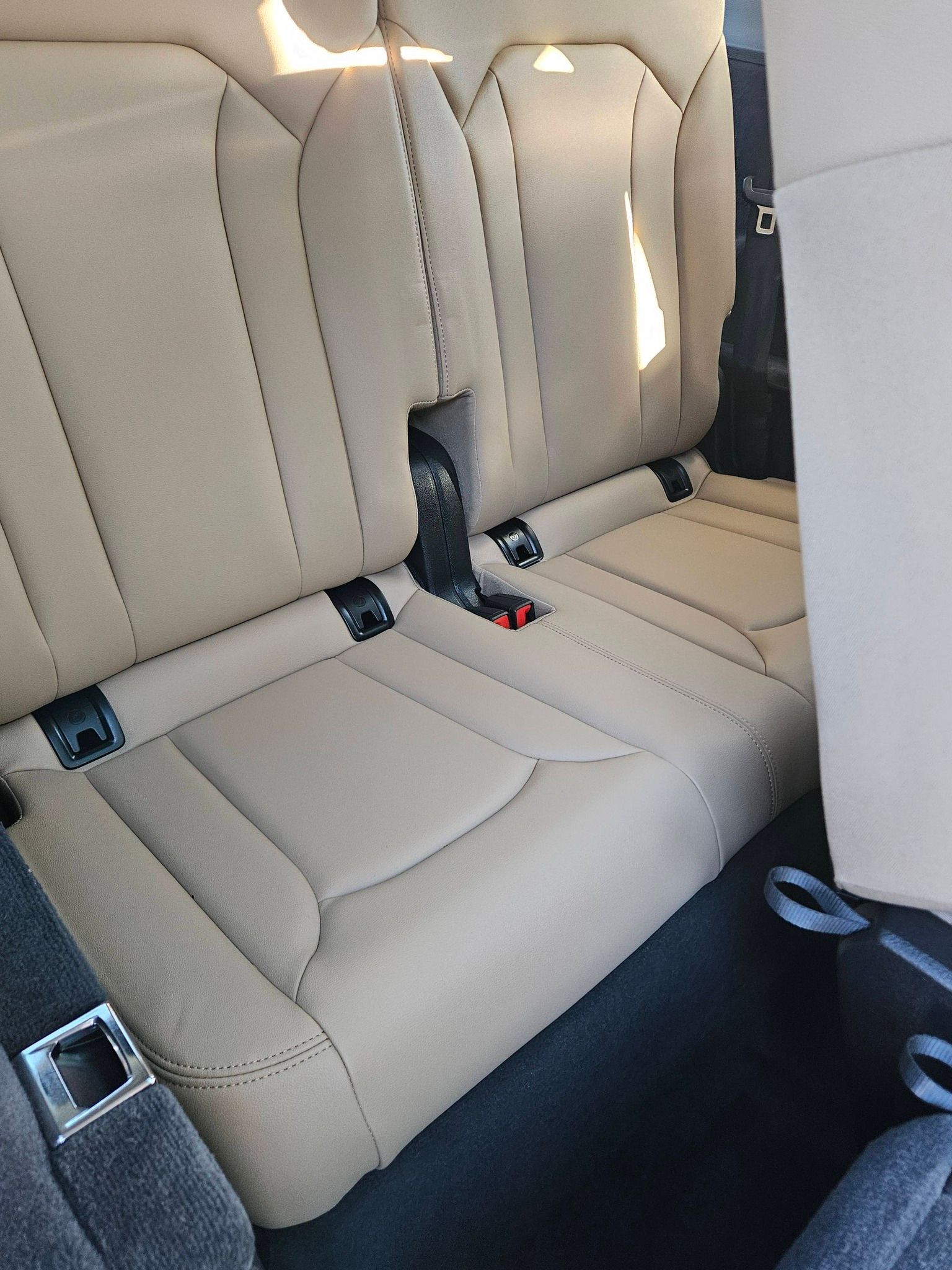 Tan-colored leather car seats in a vehicle interior with visible black safety belt buckles and floor carpeting.