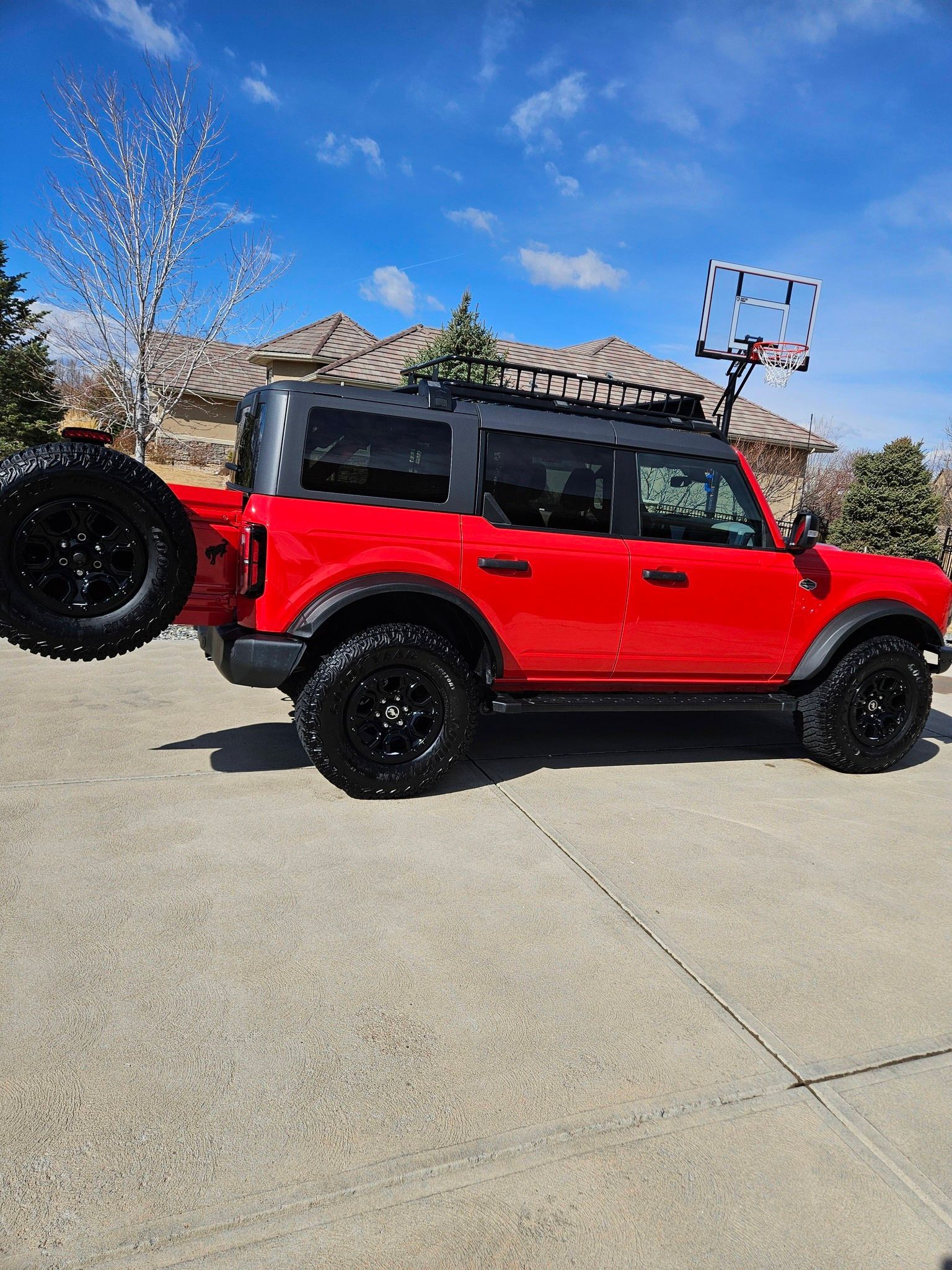 A bright red four-door Ford Bronco with black wheels and a roof rack parked on a driveway in a residential neighborhood.