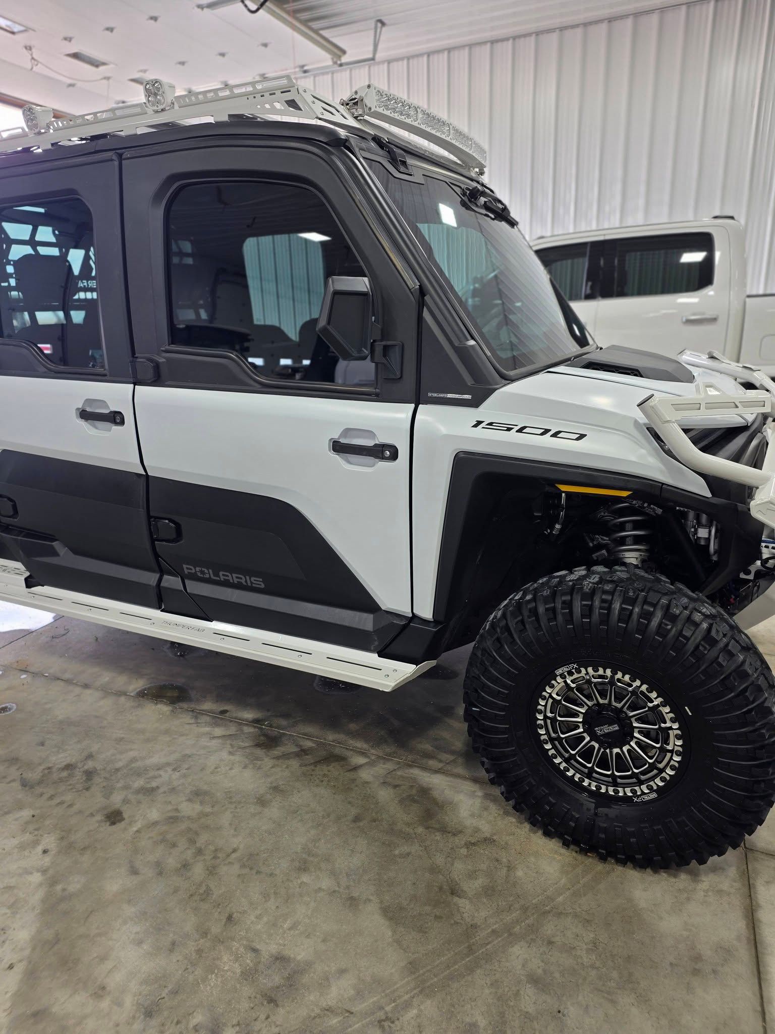 A white and black four-door Polaris off-road utility vehicle parked in an indoor garage.