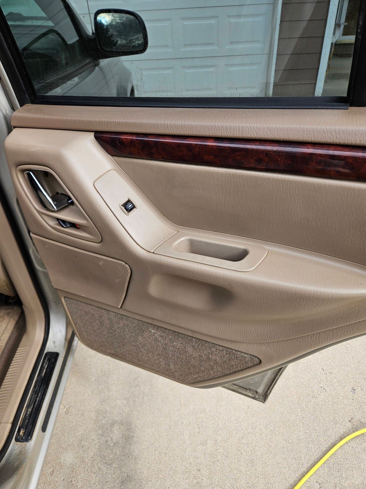 Interior view of a tan car door panel featuring a wood-grain trim accent, a window control switch, and a speaker grille.