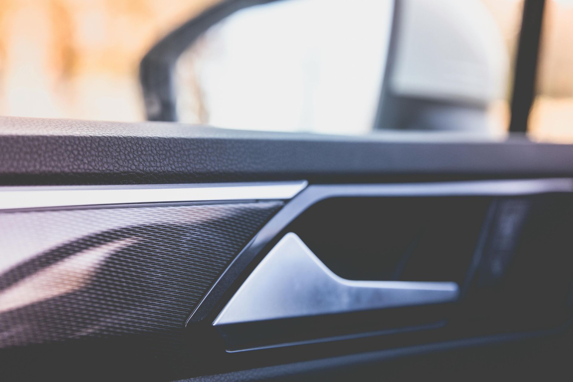 Interior view of a modern car door panel showing a metallic door handle and dark textured trim.