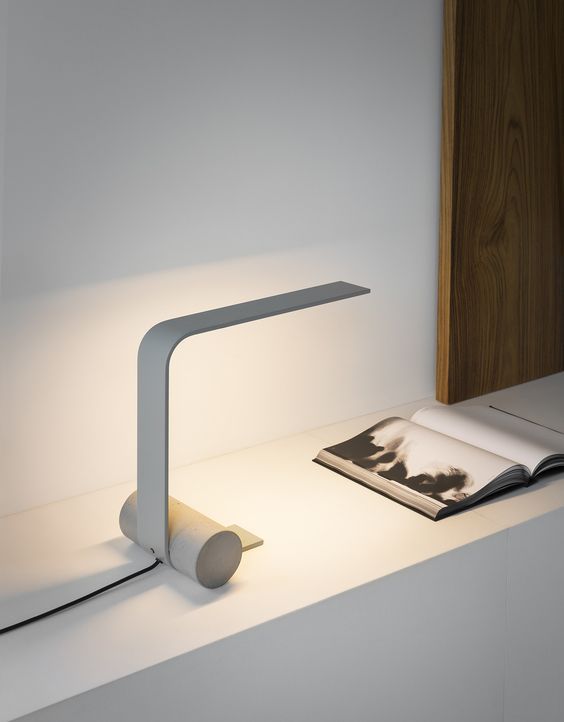 Minimalist white desk lamp illuminating an open book on a wooden surface.