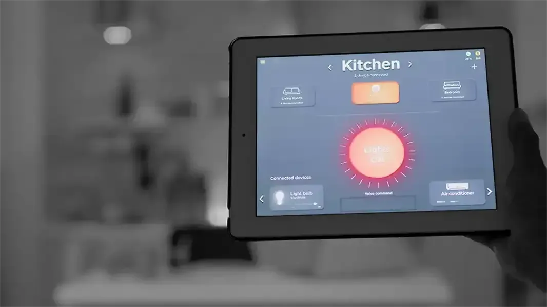 A pic of a hand holding a tablet inside a home. The tablet screen shows a light control system that is controlling the kitchen light