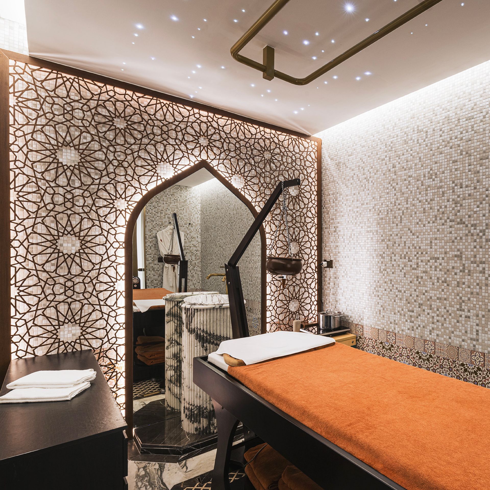 Spa room with a traditional patterned wall, featuring a marble basin and a massage bed under warm lighting.