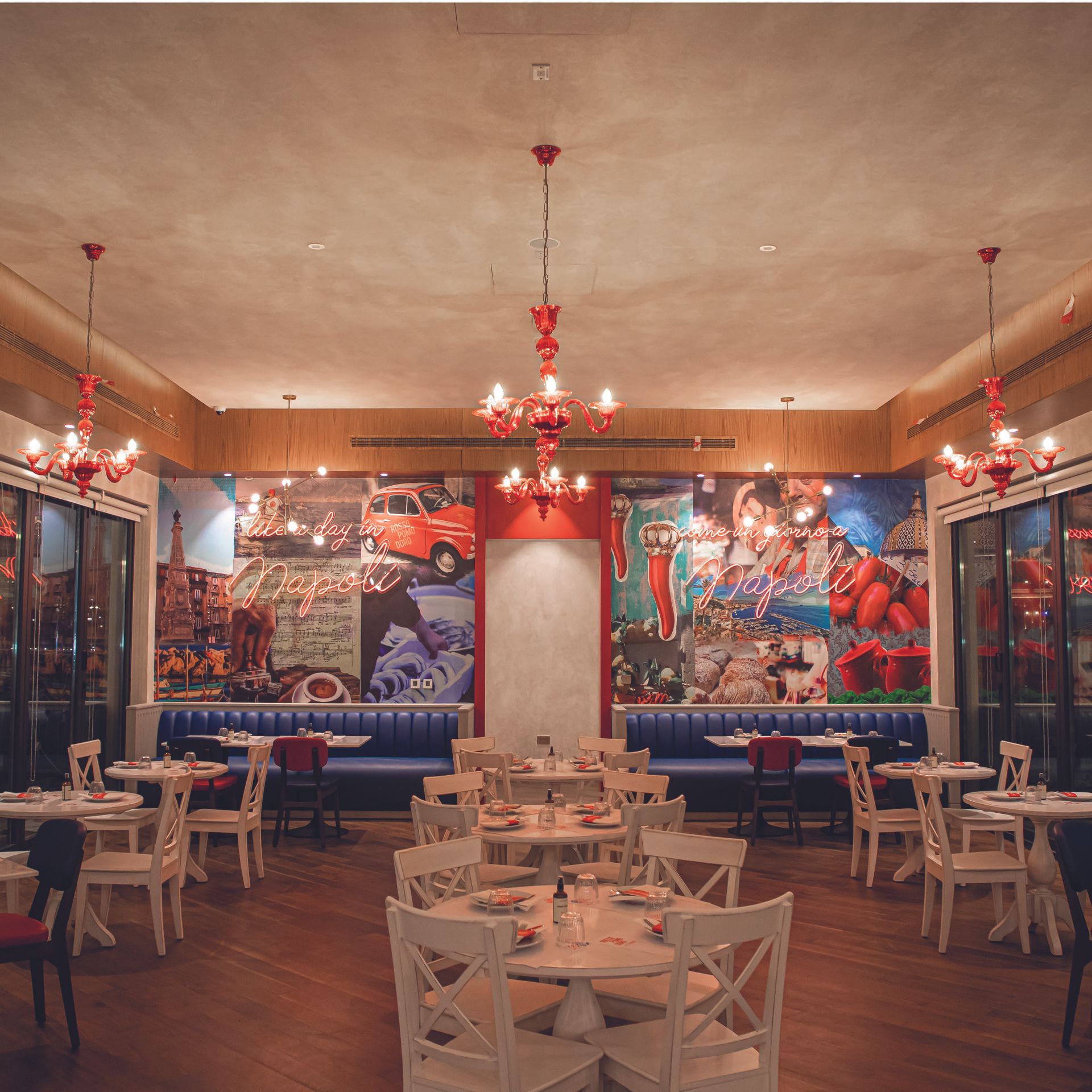 Interior of Rossopomodoro restaurant featuring vibrant wall art, red chandeliers, and neatly arranged dining tables.