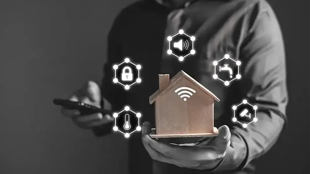 A man holding a phone in one hand and a mock-up of a house in another. Indicating that the phone can control multiple features of the house