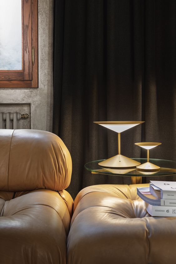 Modern gold table lamps with a layered design beside a leather armchair in a cozy room.