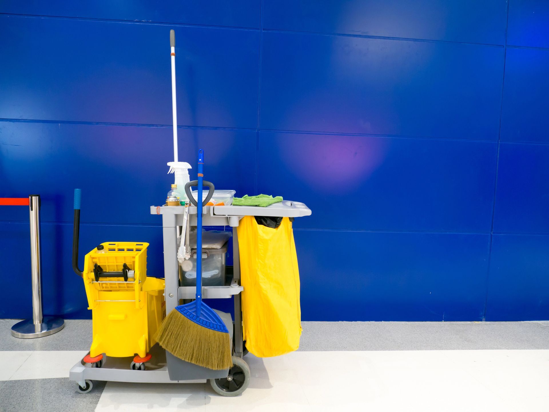Carrello per le pulizie giallo e mocio accanto a una parete blu in un corridoio