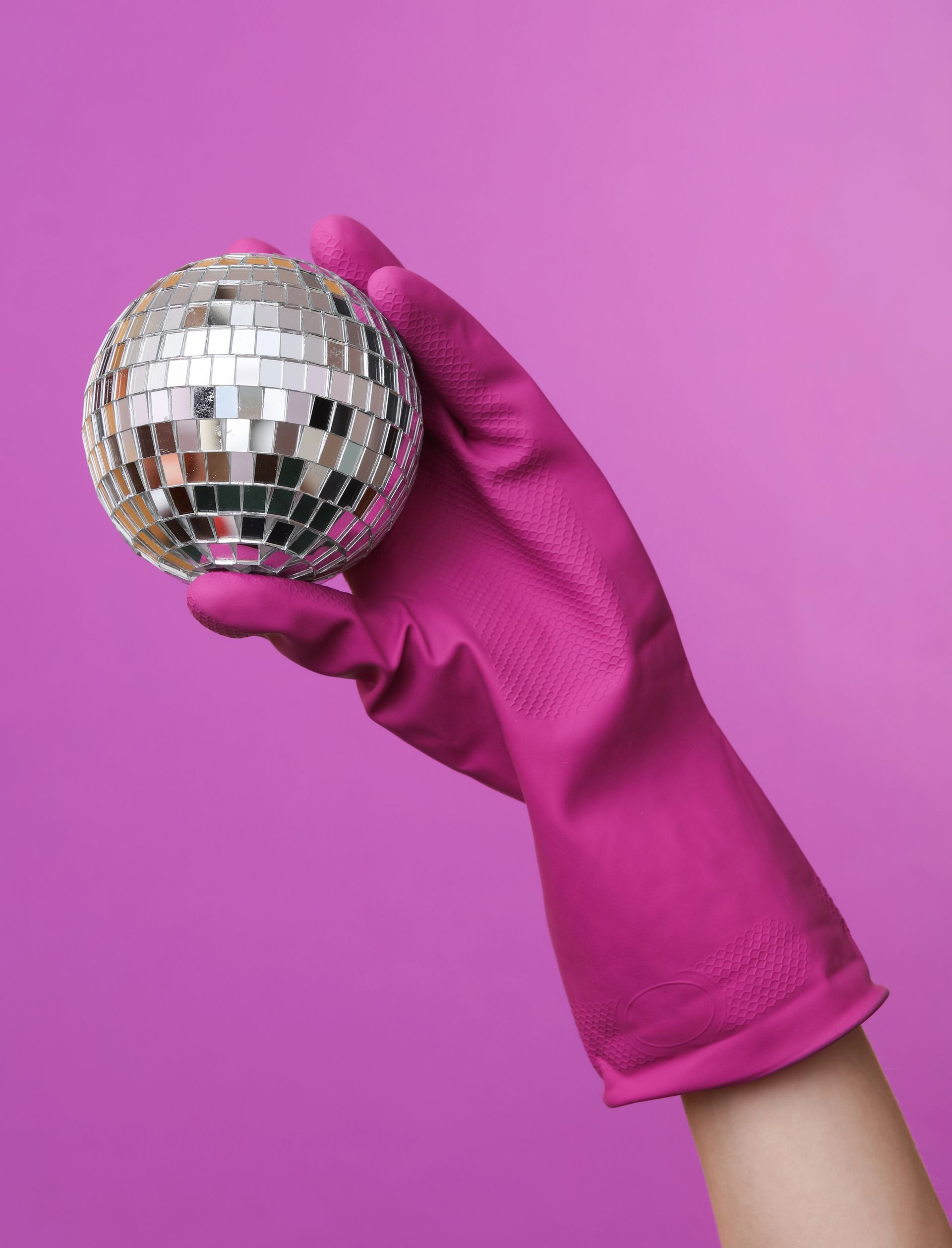 Una mano guantata di rosa che regge una piccola palla da discoteca argentata su uno sfondo rosa.