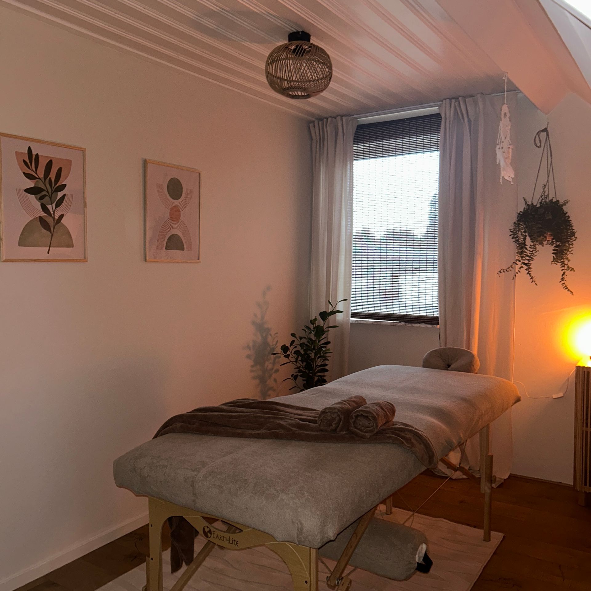 Gezellige massageruimte met behandeltafel, zachte verlichting, planten en ingelijste kunstwerken aan de muur.
