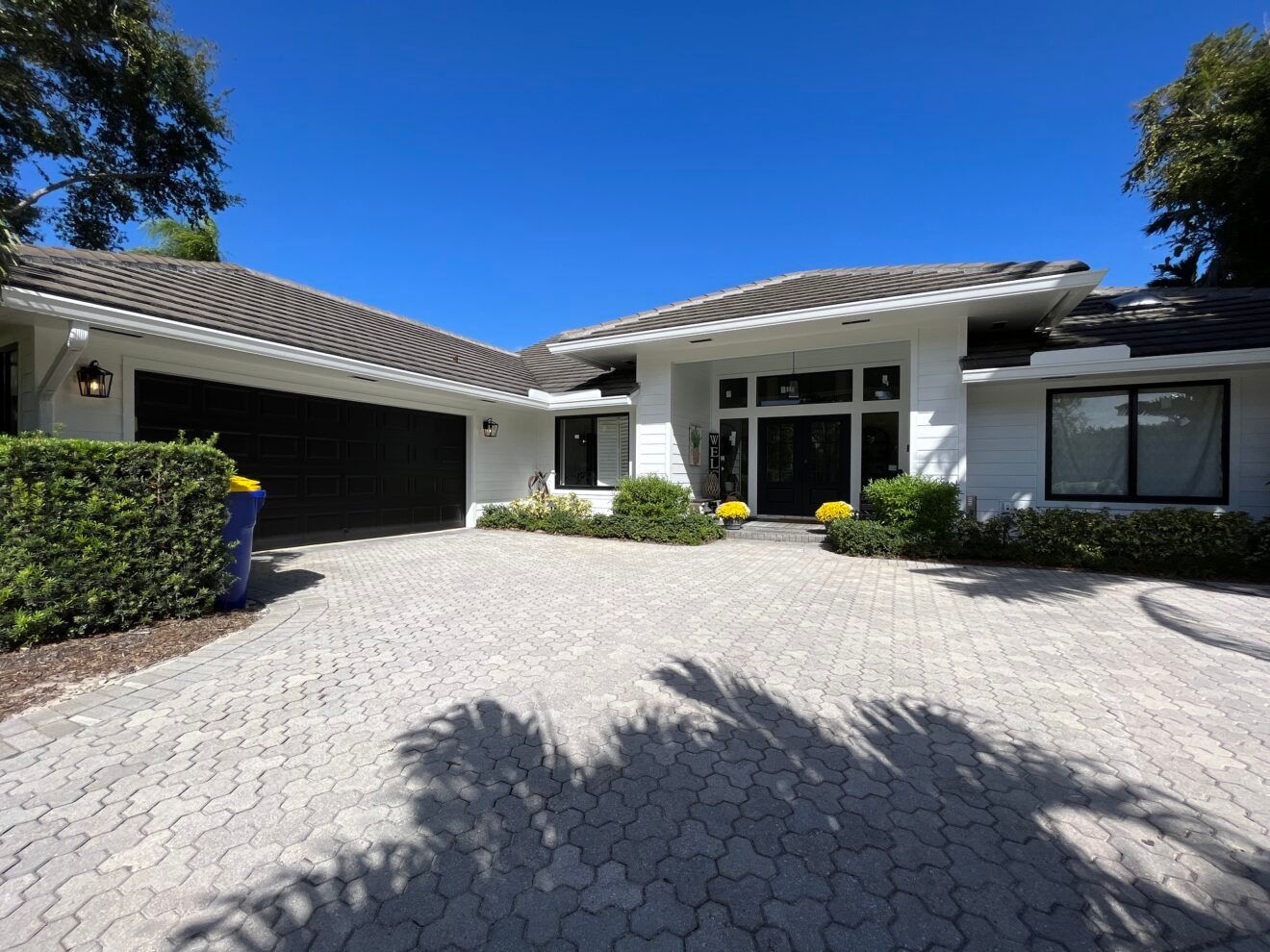 A white house with a black garage door and a brick driveway