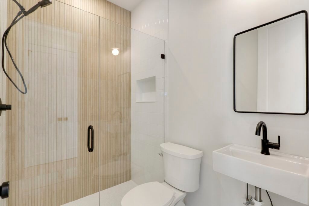 A bathroom with a toilet , sink , shower and mirror.