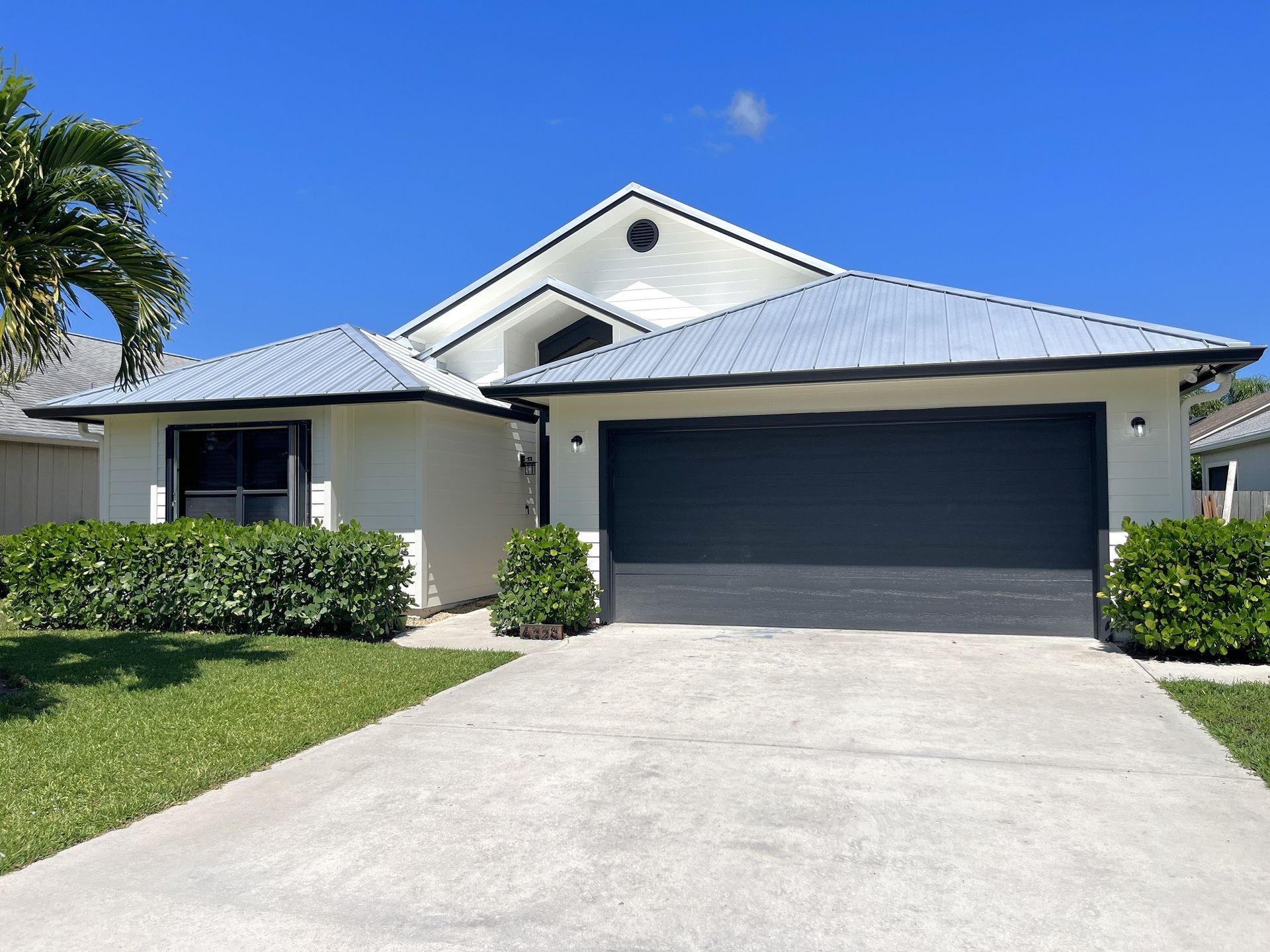A white house with a black garage door and a palm tree in front of it