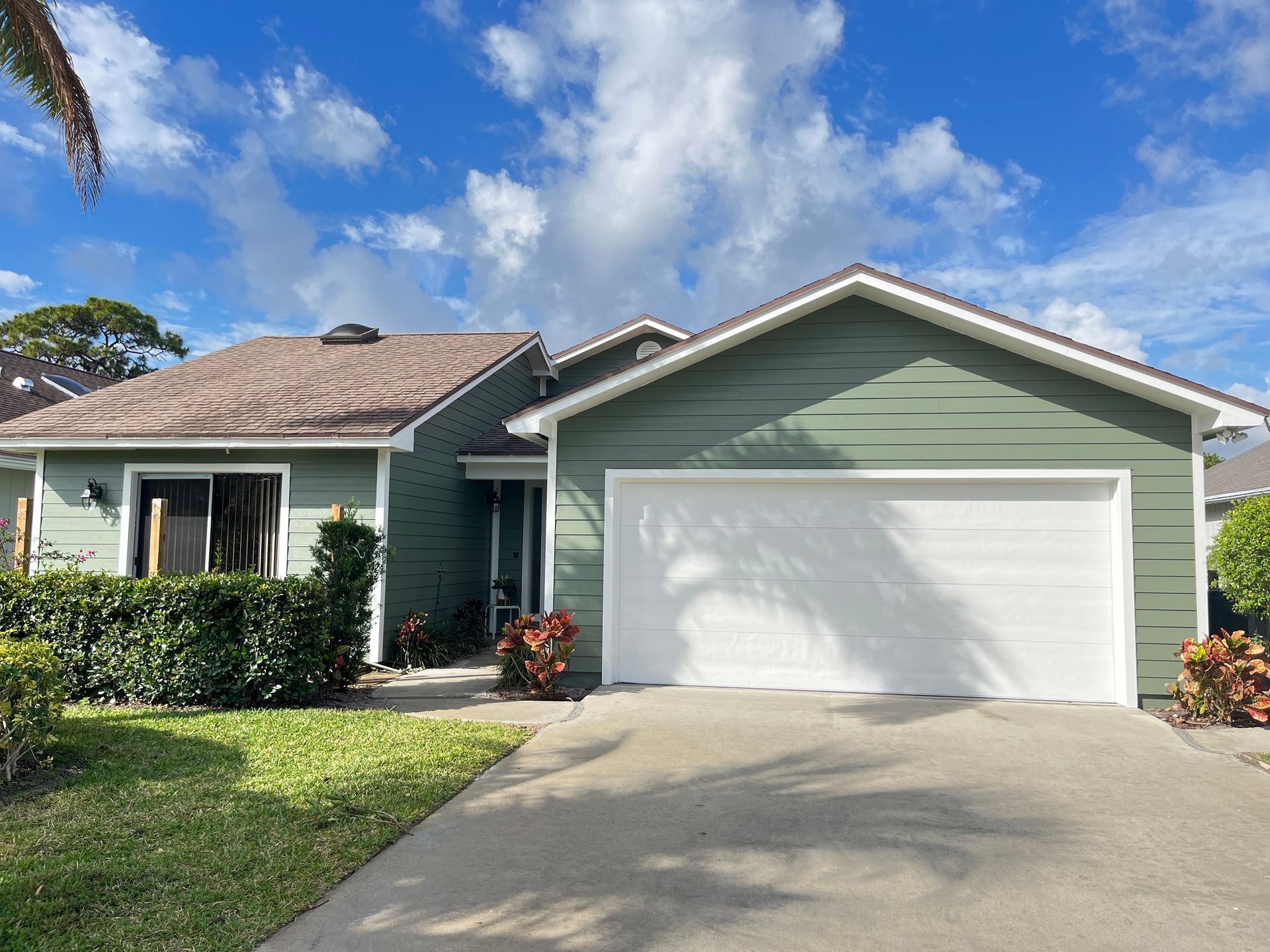 A green house with a white garage door is for sale.