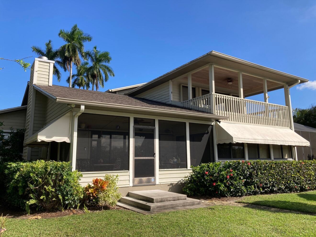 A large white house with a screened in porch and a balcony.