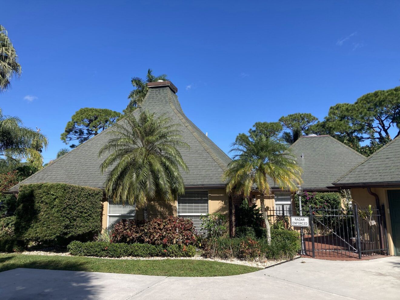 A large house with a gray roof and palm trees in front of it.