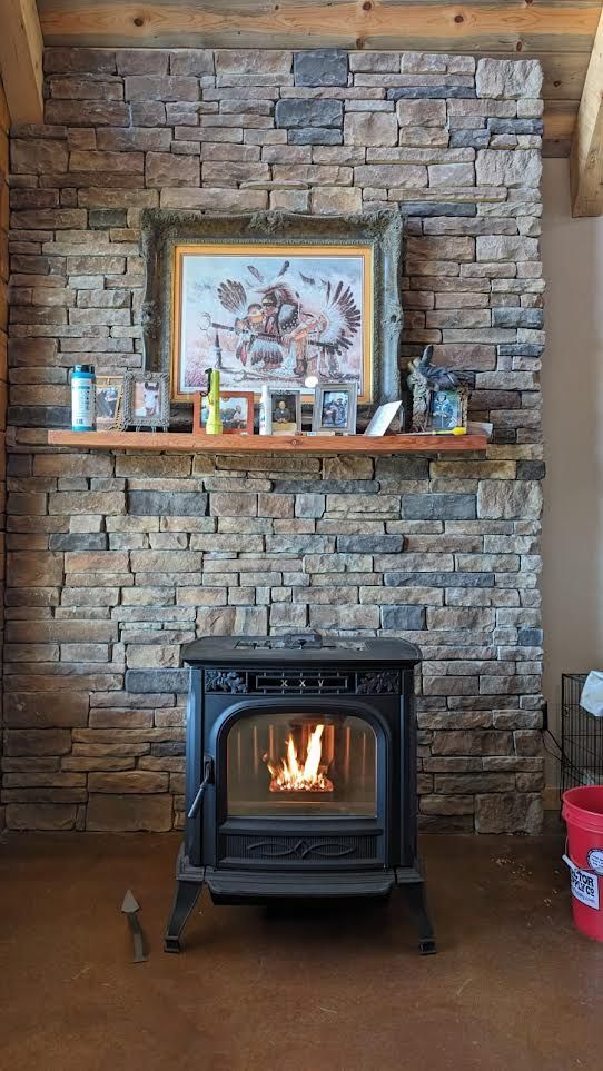 Rustic stone fireplace with a lit wood stove, mantel decor, and framed artwork above.