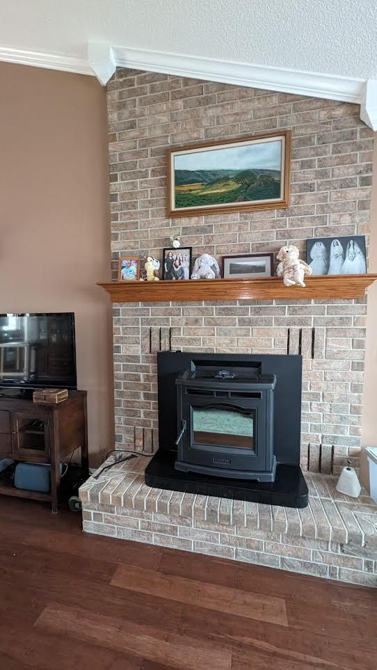 Living room fireplace with brick surround, black wood stove insert, mantel decor, and framed landscape painting.
