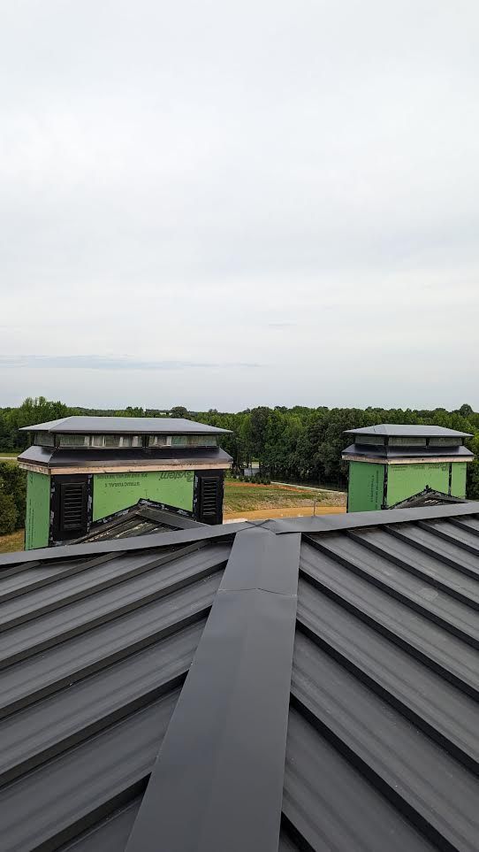 Rooftop with dark metal panels overlooking a green field and cloudy sky, with a small building in the distance