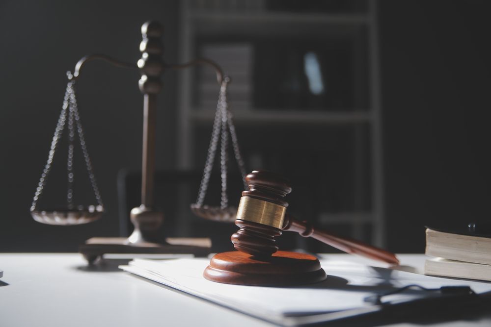 Gavel and scales of justice on white desk, lit by a dim light.