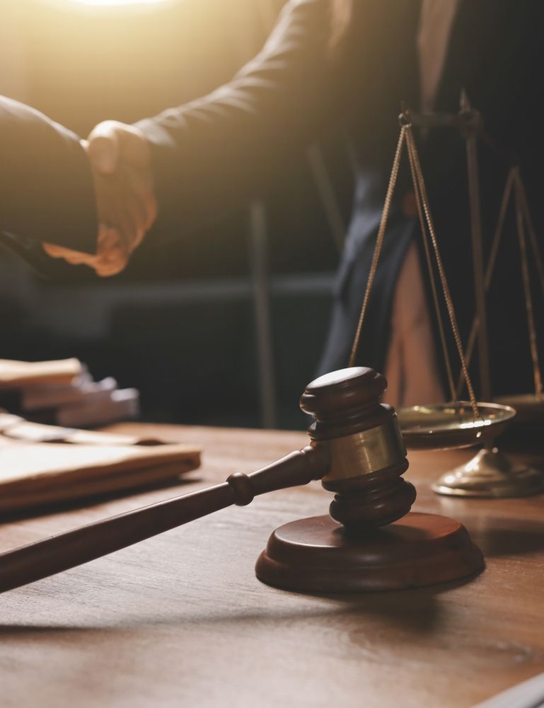 Gavel on table near scales and handshake between two people in suits.