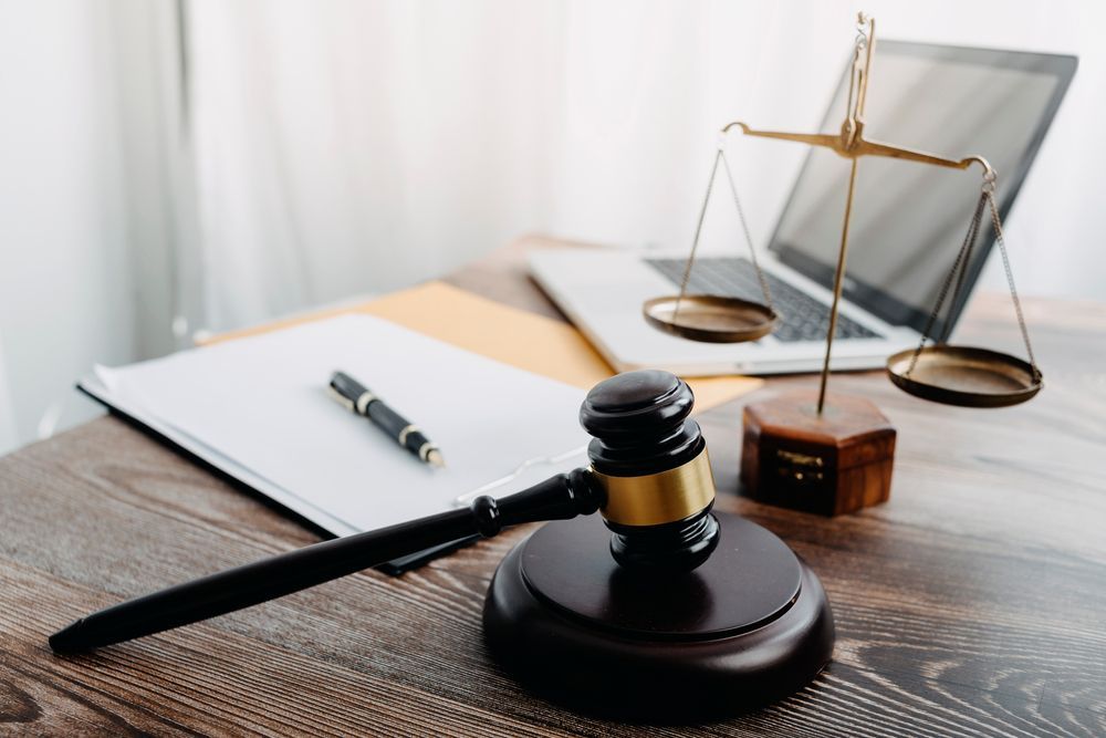 Gavel on stand with a balance scale, laptop, notepad, and pen on a wooden desk.