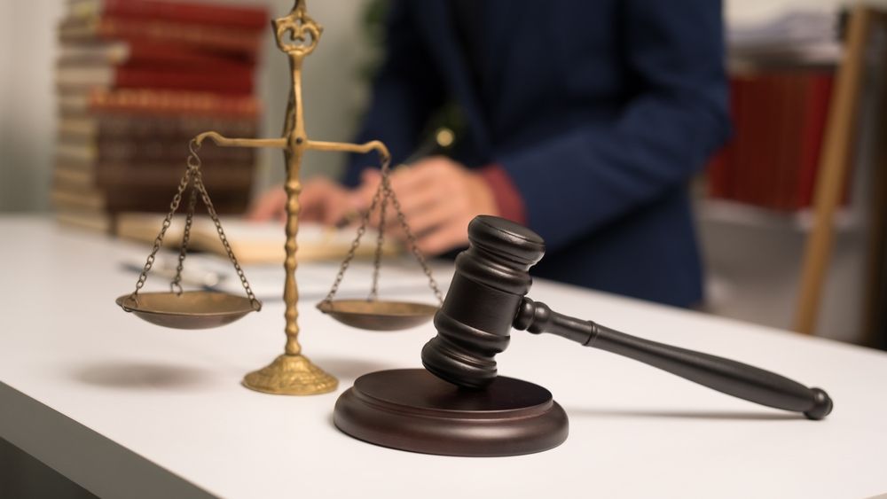Gavel and scales of justice on a desk, a person in a blue jacket works in the background.