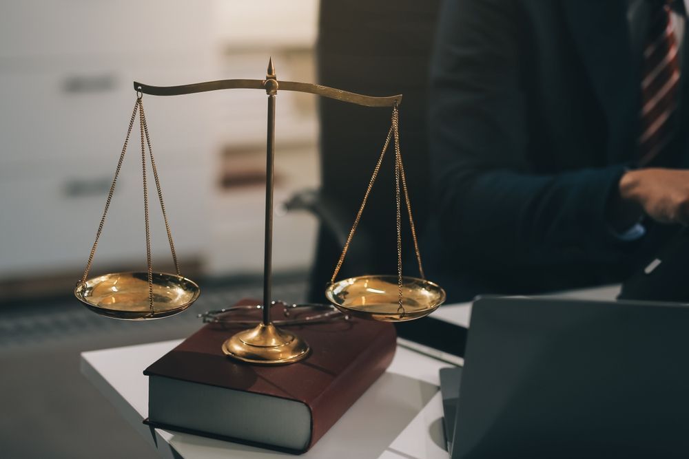 Golden scales of justice atop a law book; a person in a suit sits nearby.