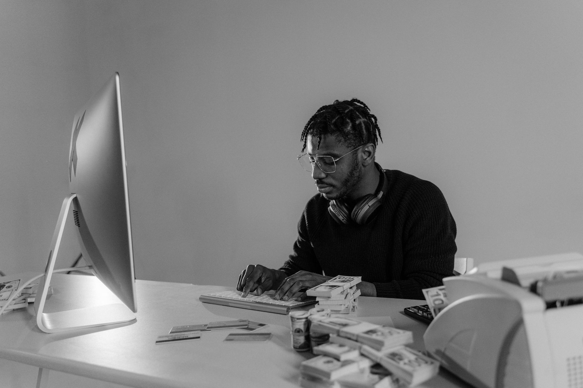 Person seated at a desk, typing on a keyboard, with money and a printer visible.