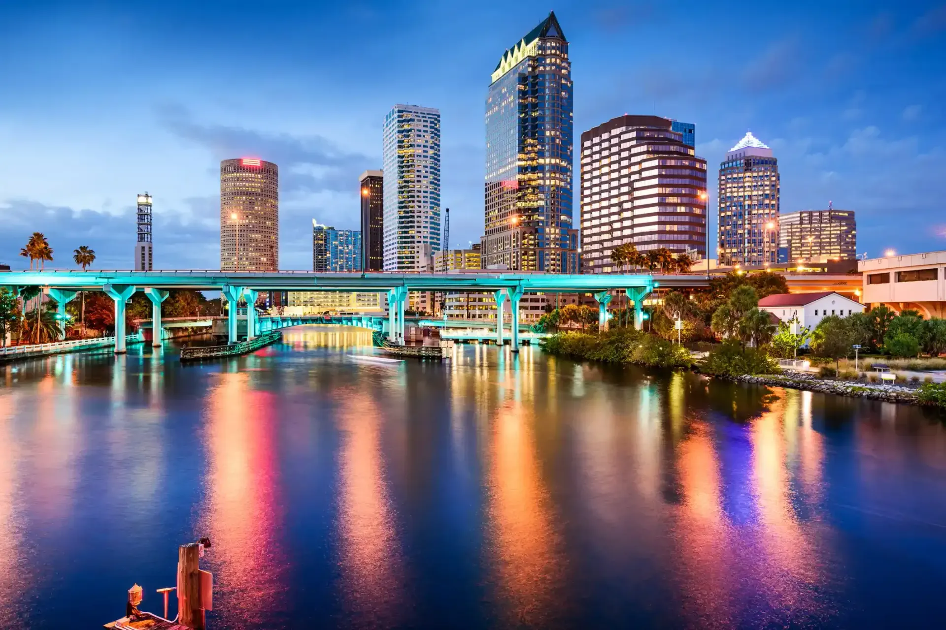 Tampa, Florida skyline at dusk, reflections on water. Illuminated bridge and city lights.