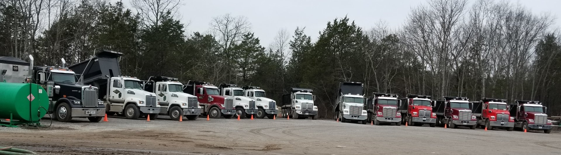 A row of trucks are parked in a parking lot with trees in the background.