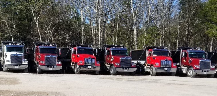 A row of dump trucks are parked in a parking lot.